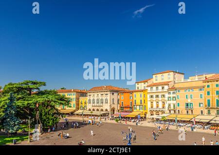 Verona, Italia, 12 de septiembre de 2019: Plaza Bra en el centro histórico de la ciudad con fila de viejos edificios coloridos cafés y restaurantes, árboles verdes y turistas caminando, cielo azul