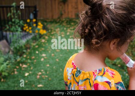 Niña con cabello rizado comiendo una paleta afuera Foto de stock