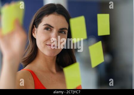 Mujer poniendo una nota pegajosa en la pared de cristal de la casa Foto de stock