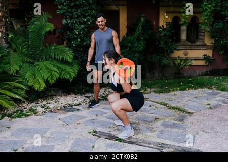 Instructor de fitness mirando a la mujer levantando pesas en el patio