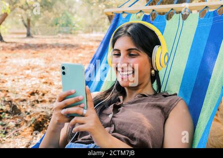 hermosa mujer con auriculares utilizando el smartphone mientras descansa en una hamaca. Foto de stock