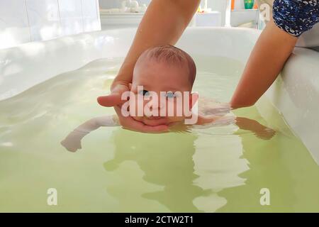 Bebé en piscina especial con instructor médico. Niños recién nacidos nadando, enseñando. Manos sosteniendo al niño en el baño