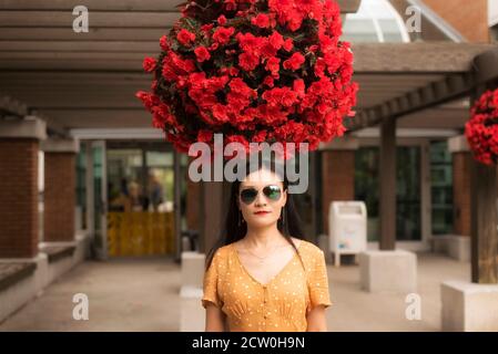 Una mujer china de pie bajo una gran olla colgante de begonias rojas en la entrada del jardín de Montreal bontanical en Montreal quebec canadá. Foto de stock