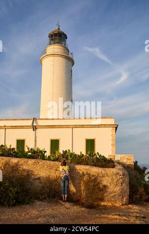 Hiker hembra fotografiando el faro de Far de la Mola contra el cielo azul en un día claro (la Mola, Formentera, Islas Pityúsic, Islas Baleares, España) Foto de stock