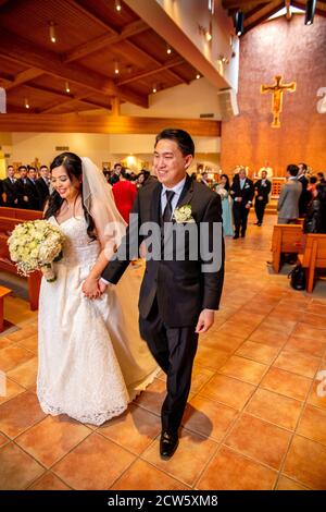 Una novia recién casada y un novio caminan por el pasillo de una iglesia católica del sur de California. Foto de stock