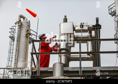 Depósito de petróleo de Zhaik-Munai, Kazajstán. Refinería de petróleo y planta de procesamiento de gas. Trabajador del petróleo (ingeniero) en overoles rojos y sombrero duro blanco en el trabajo.