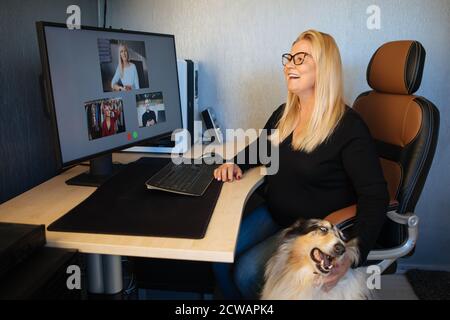Sonriente mujer madura que tiene videollamada a través de la computadora en la oficina de casa un perro collie además. Reuniones de equipo en línea videollamadas desde casa.