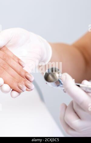 Mujer joven recibiendo manicura con aerógrafo en salón de uñas.  procedimiento para rociar pintura en las uñas.