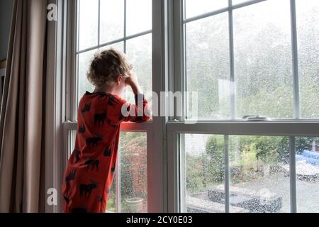 Vista trasera de joven con pelo rizado mirando hacia fuera Ventana cubierta de lluvia