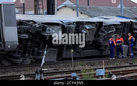 Rescue workers stand next to the wreckage of a derailed intercity train at the Bretigny-sur-Orge station near Paris July 12, 2013. An intercity train headed for the central French city of Limoges derailed south of Paris on Friday, the national rail company SNCF said. At least six people died and several dozen were injured, twenty-two of them seriously, when a regional train derailed en route from Paris to the central city of Limoges, French President announced during a visit on site.  REUTERS/Gonzalo Fuentes  (FRANCE - Tags: TRANSPORT DISASTER)