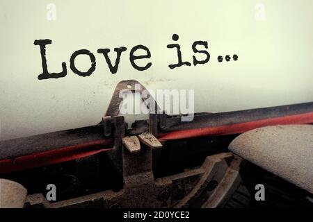 El texto escrito de primer plano 'Love is' está escrito en una hoja de papel en una máquina de escribir mecánica Foto de stock