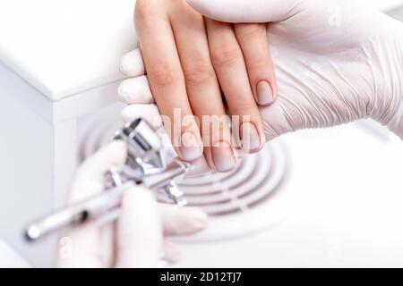 Mujer joven recibiendo manicura con aerógrafo en salón de uñas