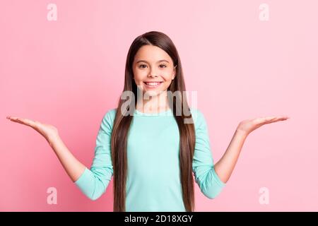 Foto de alegre encantadora y dulce pequeña dama hispana largo pelo levantar las manos sostener el espacio vacío proponer demostrar ofrece el uso de la sonrisa turquesa Foto de stock