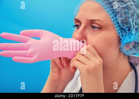 El médico infla un guante médico rosa, de cerca sobre un fondo azul. Enfermera llena un guante protector con aire, concepto Foto de stock