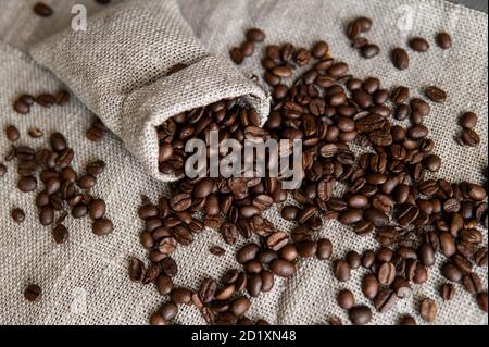 Café disperso de una bolsa de lino y una taza de café negro Espresso o  Americano de pie sobre una mesa de madera. Granos de café arábica frescos  en la ropa de