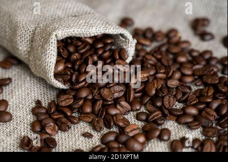 Café disperso de una bolsa de lino y una taza de café negro Espresso o  Americano de pie sobre una mesa de madera. Granos de café arábica frescos  en la ropa de