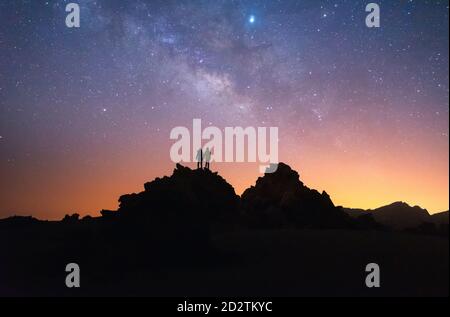 Silueta de un par de excursionistas de pie en roca oscura contra Cielo nocturno estrellado en larga exposición en Tenerife