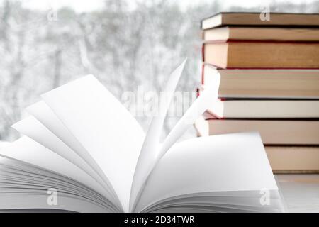 Páginas blancas y limpias de libro abierto con el telón de fondo de libros viejos y bosque de invierno