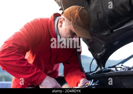 Hermoso auto mecánico o trabajador de asistencia en carretera en uniforme de reparar el motor del coche rotos en la carretera