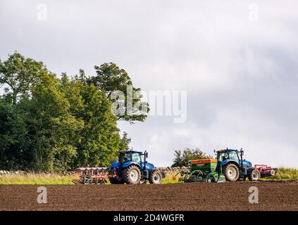 Tractores en campo arado con maquinaria de labranza, East Lothian, Escocia, Reino Unido Foto de stock
