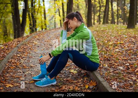 Corredor agotado que tiene descanso después de entrenar en el parque otoñal. Mujer cansada sosteniendo una botella de agua. Estilo de vida deportivo