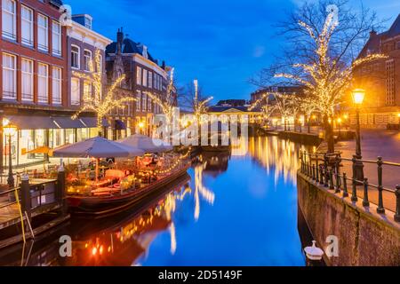 Antigua vista del canal holandés Oude Rijn con puente, edificios históricos y luces de Navidad en el centro de la ciudad de Leiden, Holanda