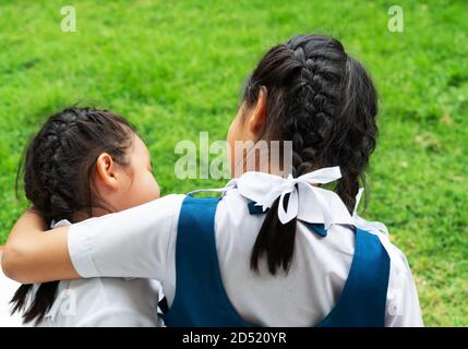 Dos pequeños asian girls hermanas abrazos feliz post en uniforme escolar, concepto de vuelta a la escuela Foto de stock