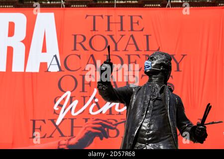 Londres, Reino Unido. - 5 de octubre de 2020: Una estatua enmascarada frente a una bandera que anuncia la tradicional exposición de verano de la Real Academia, retrasada hasta octubre debido a la pandemia del coronavirus.