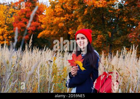 Mujer con pelo largo y sonrisa atractiva de pie en el campo de otoño con bosque colorido sobre el fondo. Foto de stock