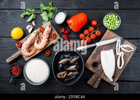 Especialidades de marisco fresco sin cocinar y arroz con mejillones, gambas y calamares sobre fondo de madera negra, sobre una base plana Foto de stock