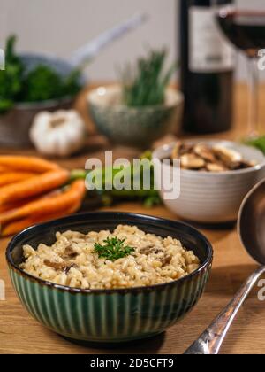 Cuenco de risotto sobre una mesa con ingredientes, setas, ajo, zanahorias y una copa de vino. Foto de stock