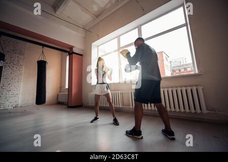Un hombre y una mujer que escatiman compañeros se entrenan en el sala de entrenamiento de combatientes en guantes de boxeo con patas