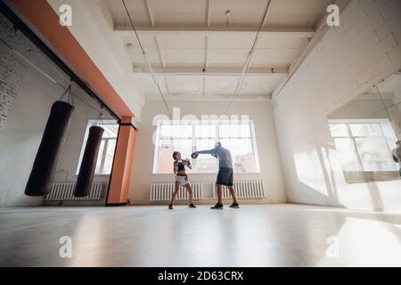 Un hombre y una mujer que escatiman compañeros se entrenan en el sala de entrenamiento de combatientes en guantes de boxeo con patas