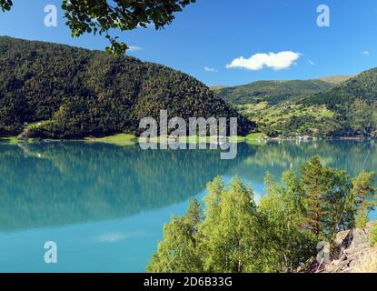 Montañas que se reflejan en el hermoso agua Turquesa del Lustrafjord En un soleado día de verano con un cielo azul claro Y algunas Nubes Foto de stock