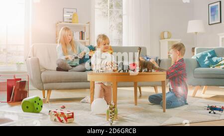 En casa: Cute Girl jugando en Video Game Console, usando Joystick Controller, su joven Brothe juega con Toy Airplane y la hermana más joven juega con Foto de stock