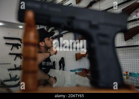 Najaf, Irak. 19 de octubre de 2020. Un traficante de armas se encuentra entre una colección exhibida de rifles y pistolas en una tienda que vende armas de fuego y municiones, donde se permite a las personas comprar armas autorizadas después de emitir los permisos necesarios de las autoridades de seguridad. Crédito: Ameer al Mohammedaw/dpa/Alamy Live News Foto de stock