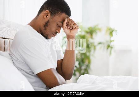 Hombre afroamericano sufriendo depresión sentado en la cama en casa Foto de stock