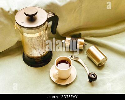 Prensa francesa, taza de café con expreso caliente oscuro en el platillo y  un pequeño molinillo de café de metal en tela verde claro. Vida quieto.  Elaboración de coff fresco Fotografía de stock - Alamy