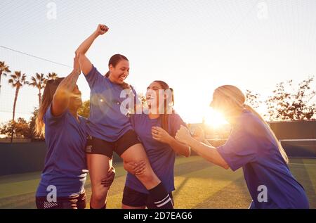 Equipo de fútbol femenino celebrando el partido de fútbol ganador levantando a jugador en Hombros