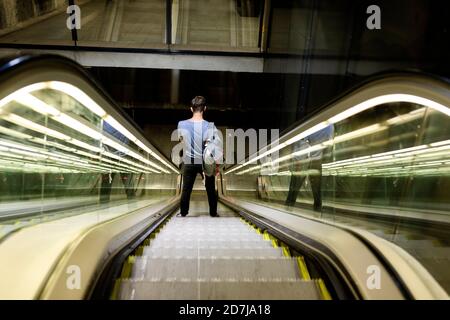 Joven con mochila de pie en escalera mecánica iluminada en el metro Foto de stock