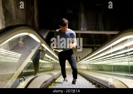 Hombre que usa el teléfono inteligente mientras está parado en la escalera mecánica metro Foto de stock