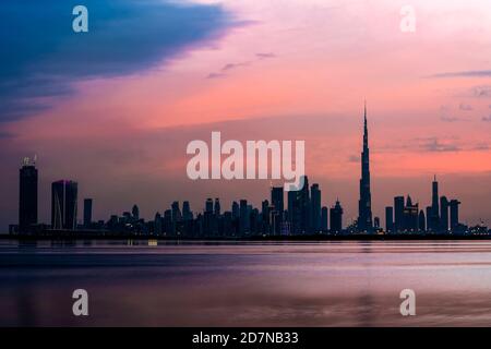 Vista impresionante del horizonte iluminado de Dubai al atardecer con el magnífico Burj Khalifa y el canal de agua que fluye en primer plano. Foto de stock