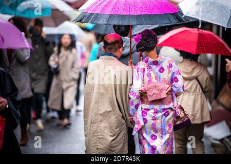 Kyoto, Japón - 10 de abril de 2019: Gente candida detrás de mujer y hombre sosteniendo paraguas vestido con traje de kimono durante el día lluvioso en la calle ne Foto de stock
