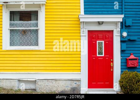 Una puerta roja brillante de un edificio con paredes de clapboard de madera azul y amarilla. La casa tiene un buzón de metal decorativo rojo.
