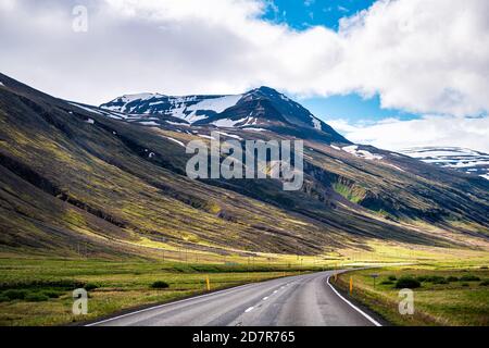Vista de las montañas nevadas al oeste de Akureyri con azul cielo durante el soleado día de verano y carretera de circunvalación asfaltada autopista en Islandia Foto de stock