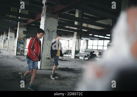 Adolescentes chicos en el interior en edificio abandonado, caminar. Foto de stock