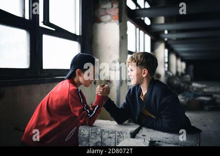 Adolescentes chicos en el interior en edificio abandonado, lucha de brazos. Foto de stock