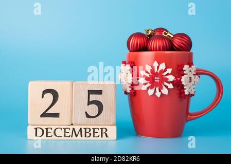 Feliz concepto de celebración. Foto de cerca del calendario de madera que muestra el 25 de diciembre y una copa de colores vivos llena de pequeñas bolas de juguete árbol aislado ov