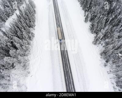 Camino de semirailer conduciendo a través de la ventisca en la carretera de invierno, vista superior desde el drone en invierno Foto de stock