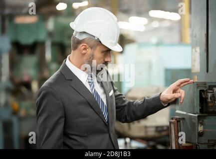 El director de hipster barbudo con sombrero de ingeniero de pie contra el cnc máquina en producción en fábrica Foto de stock